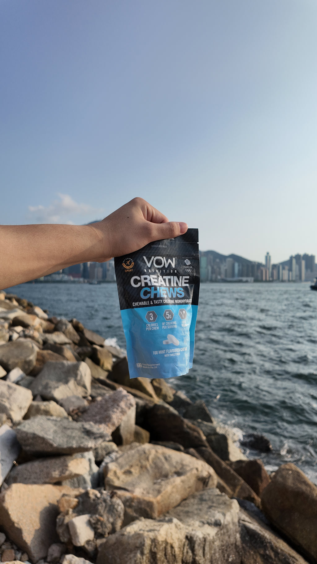 A hand holding VOW Mint Creatine Chews by a rocky waterfront