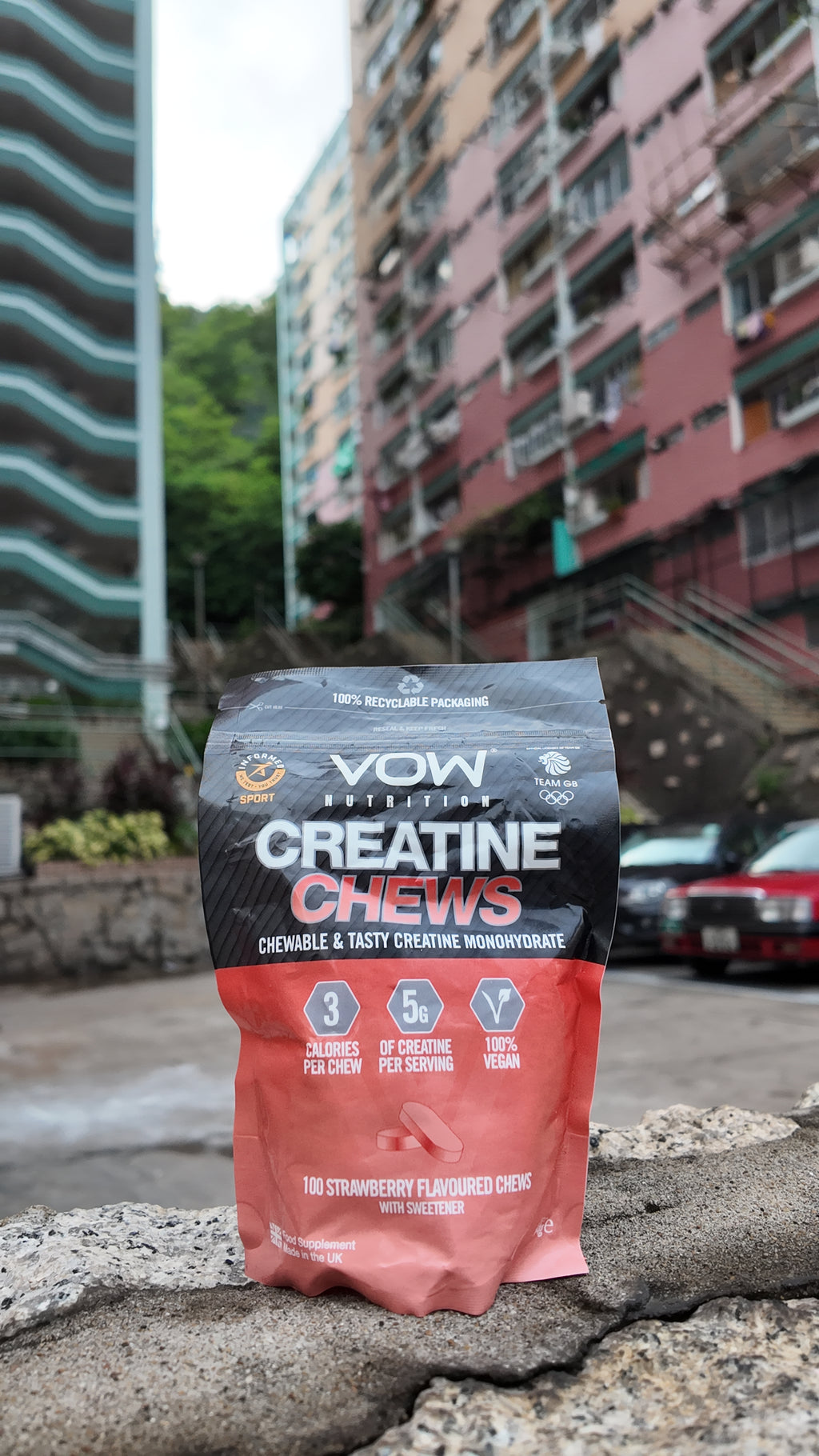VOW Strawberry Creatine Chews on a stone ledge with Hong Kong residential buildings behind