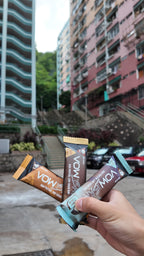 A hand holding VOW Salted Caramel, Peanut Crunch and Cookies and Cream bars in a Hong Kong street