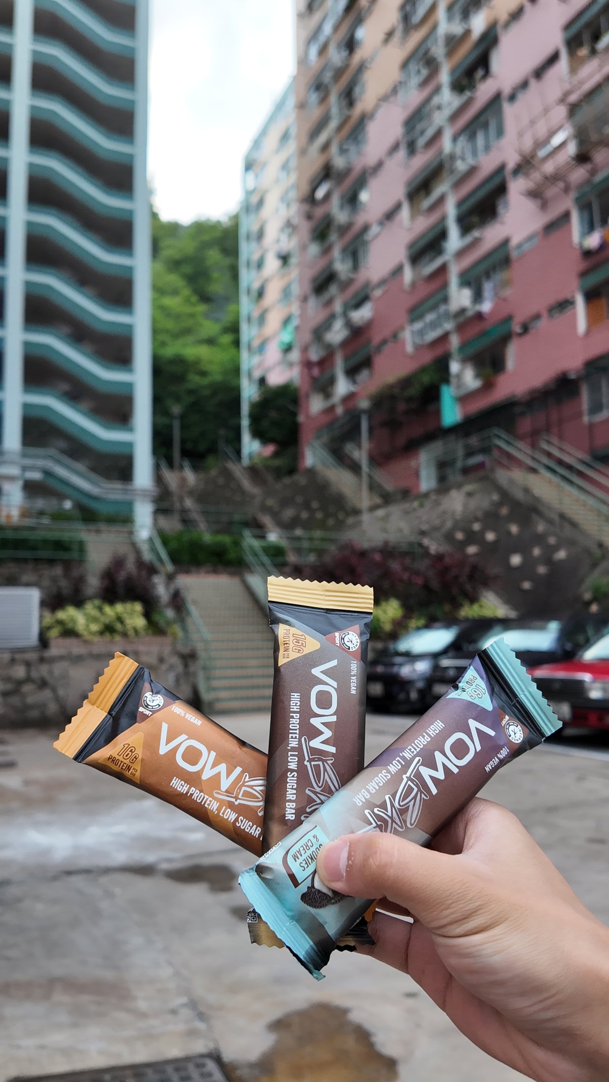A hand holding VOW Salted Caramel, Peanut Crunch and Cookies and Cream bars in a Hong Kong street