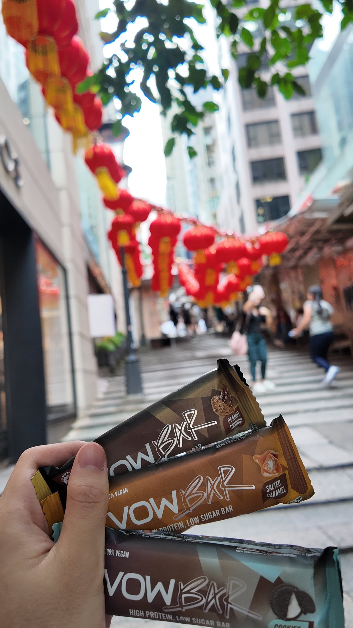 VOW Salted Caramel, Peanut Crunch and Cookies and Cream bars held in front of stone steps and red lanterns